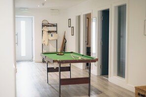 Una habitación con mesa de billar, una puerta que da a otra habitación y un pasillo con puertas.