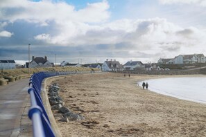 Una playa arenosa con una barrera azul curva, una hilera de casas blancas y un cielo despejado.