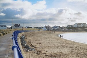 Una playa arenosa con una barrera azul curva, una hilera de casas blancas y un cielo despejado.