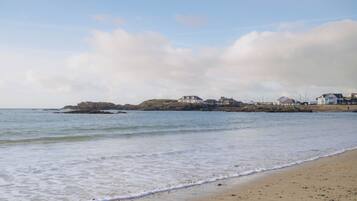 A beach with a rocky outcrop in the distance, a sandy shore, and a row of buildings along the coastline.