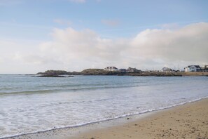 A beach with a rocky outcrop in the distance, a sandy shore, and a row of buildings along the coastline.