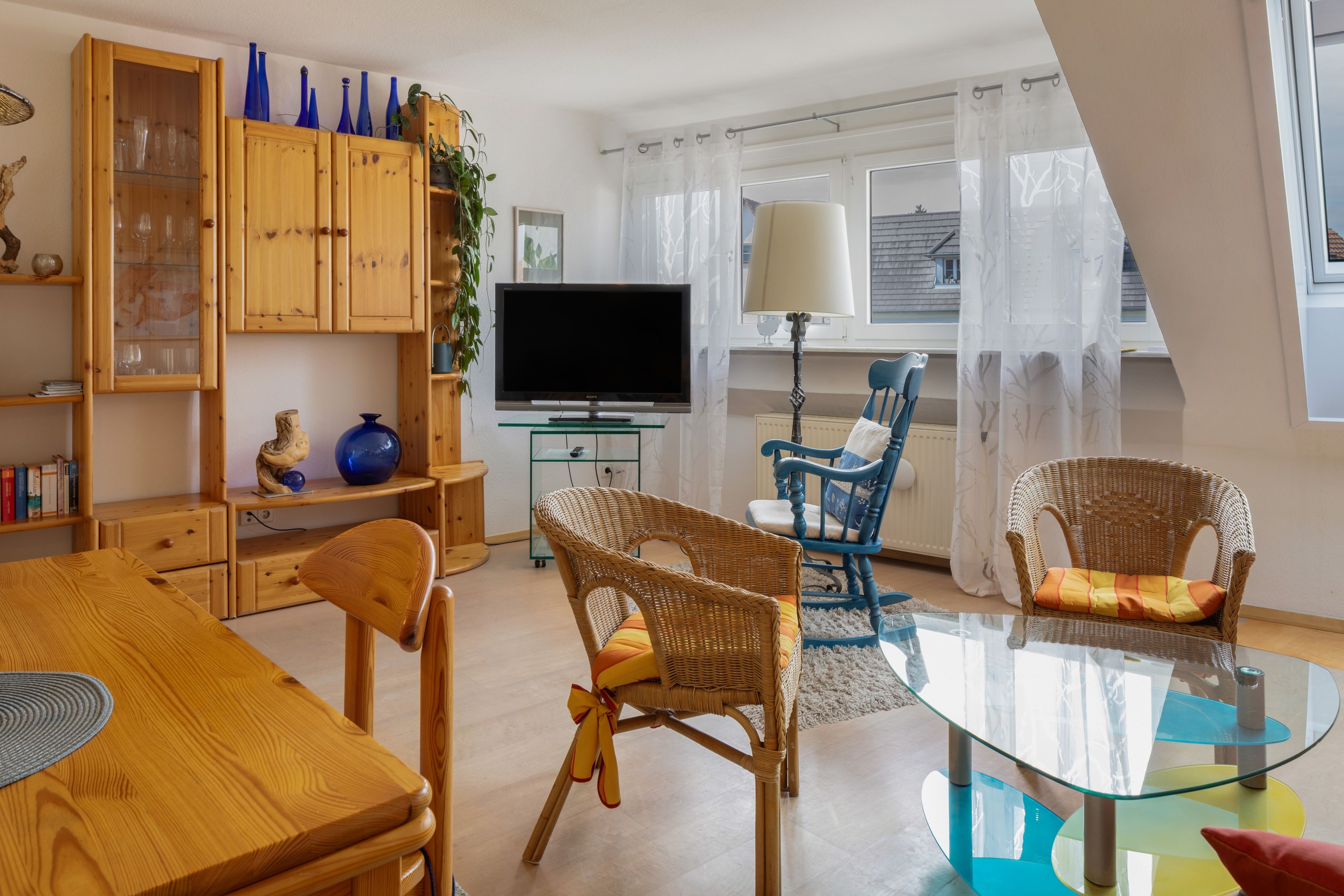 Una sala de estar moderna con un mueble de madera, un televisor de pantalla plana, sillas de mimbre y una mesa de centro de vidrio.