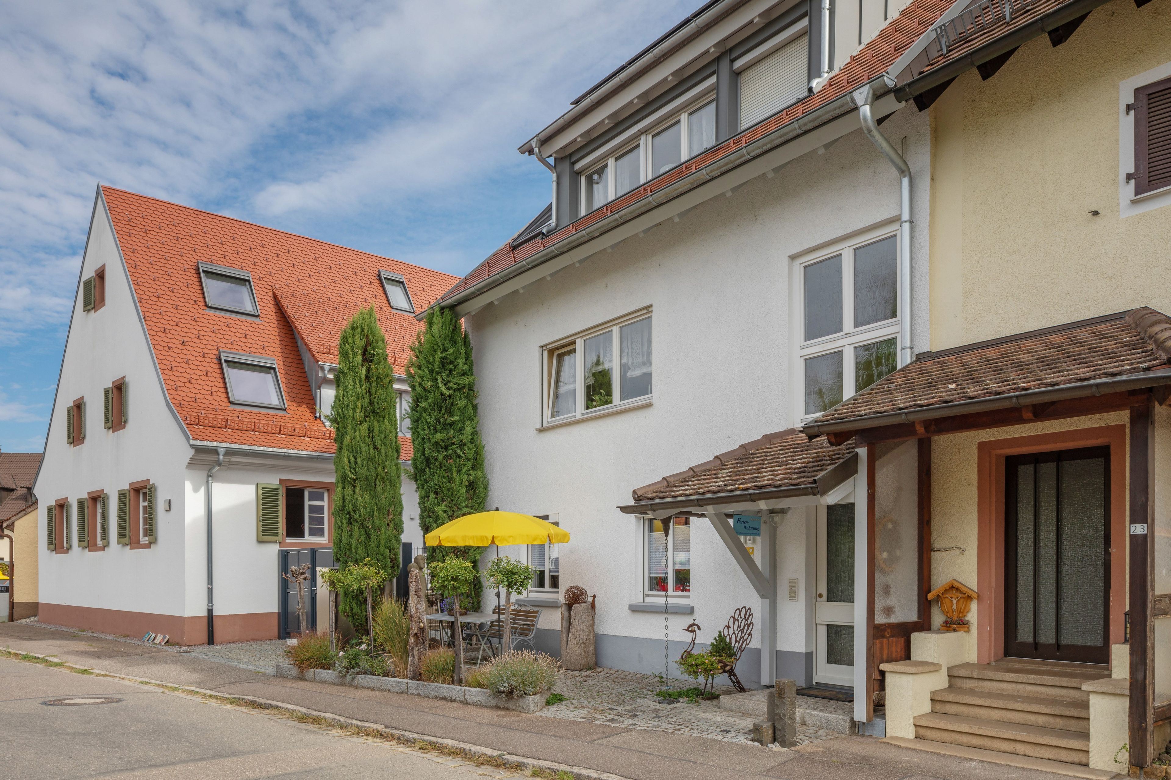 Ein Wohngebäude mit Satteldach, zahlreichen Fenstern und einer kleinen Veranda.