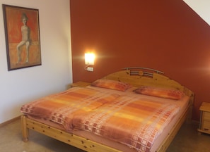 Un dormitori amb llit de fusta, una làmpada penjada a la paret i un quadre.