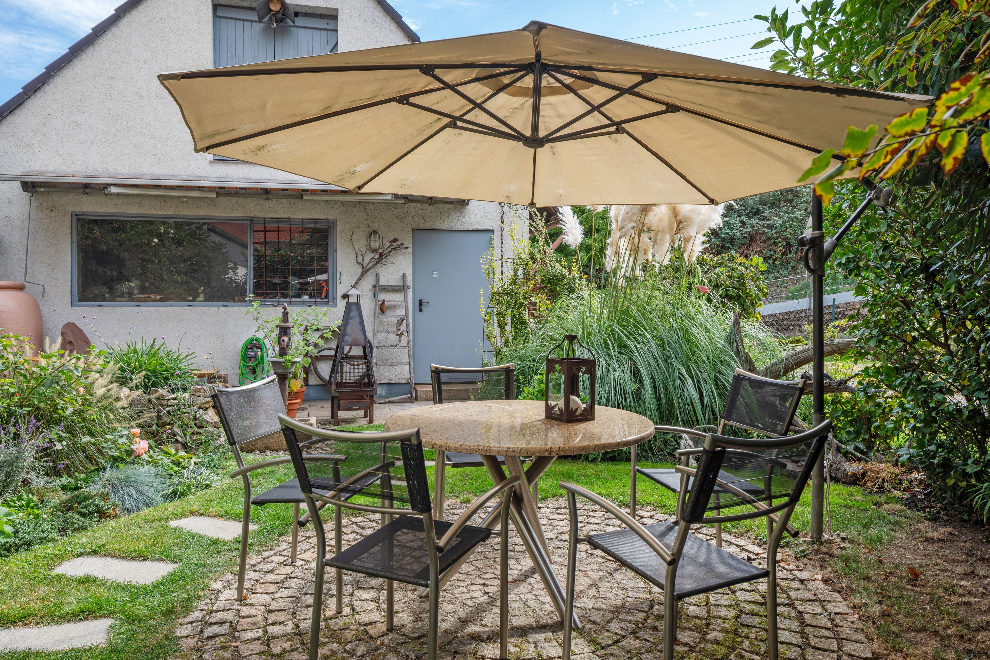 Eine Terrasse mit einem runden Tisch, Stühlen, einem Sonnenschirm und einem Vogelkäfig.