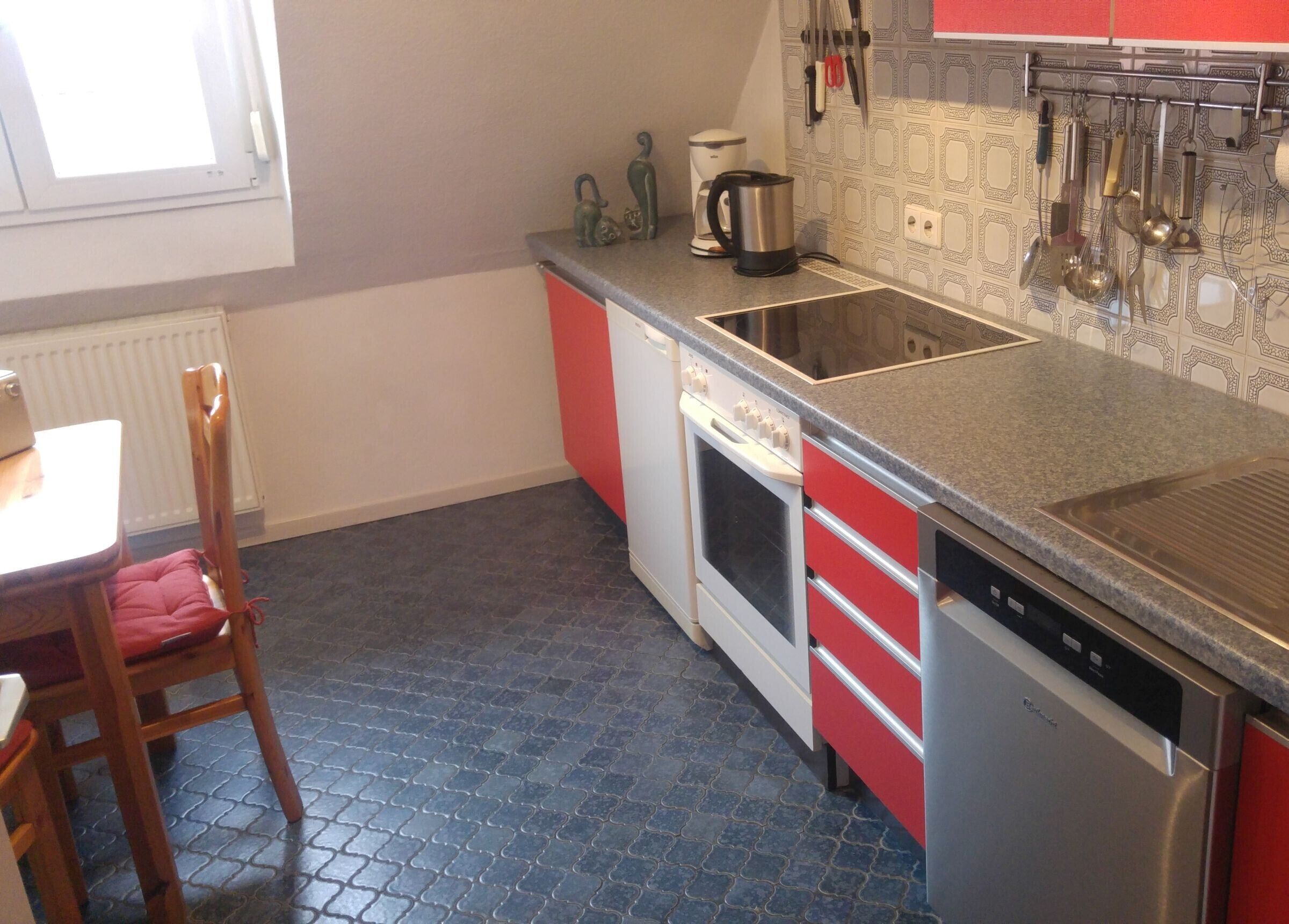 A kitchen with a red and white color scheme, a stove, a dishwasher, and a coffee maker.