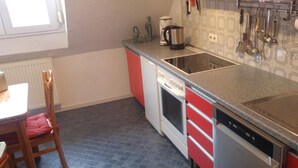 A kitchen with a red and white color scheme, a stove, a dishwasher, and a coffee maker. - Apartment Marlies in Freiburg (Freiburg im Breisgau)