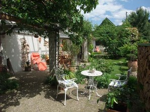 Un pati jardí amb taula i cadires, envoltat de vegetació i una paret de pedra.