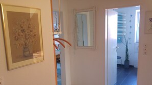 A hallway with a framed artwork, a mirror, and a door leading to a room with a plant and a window. - Apartment Marlies in Freiburg (Freiburg im Breisgau)