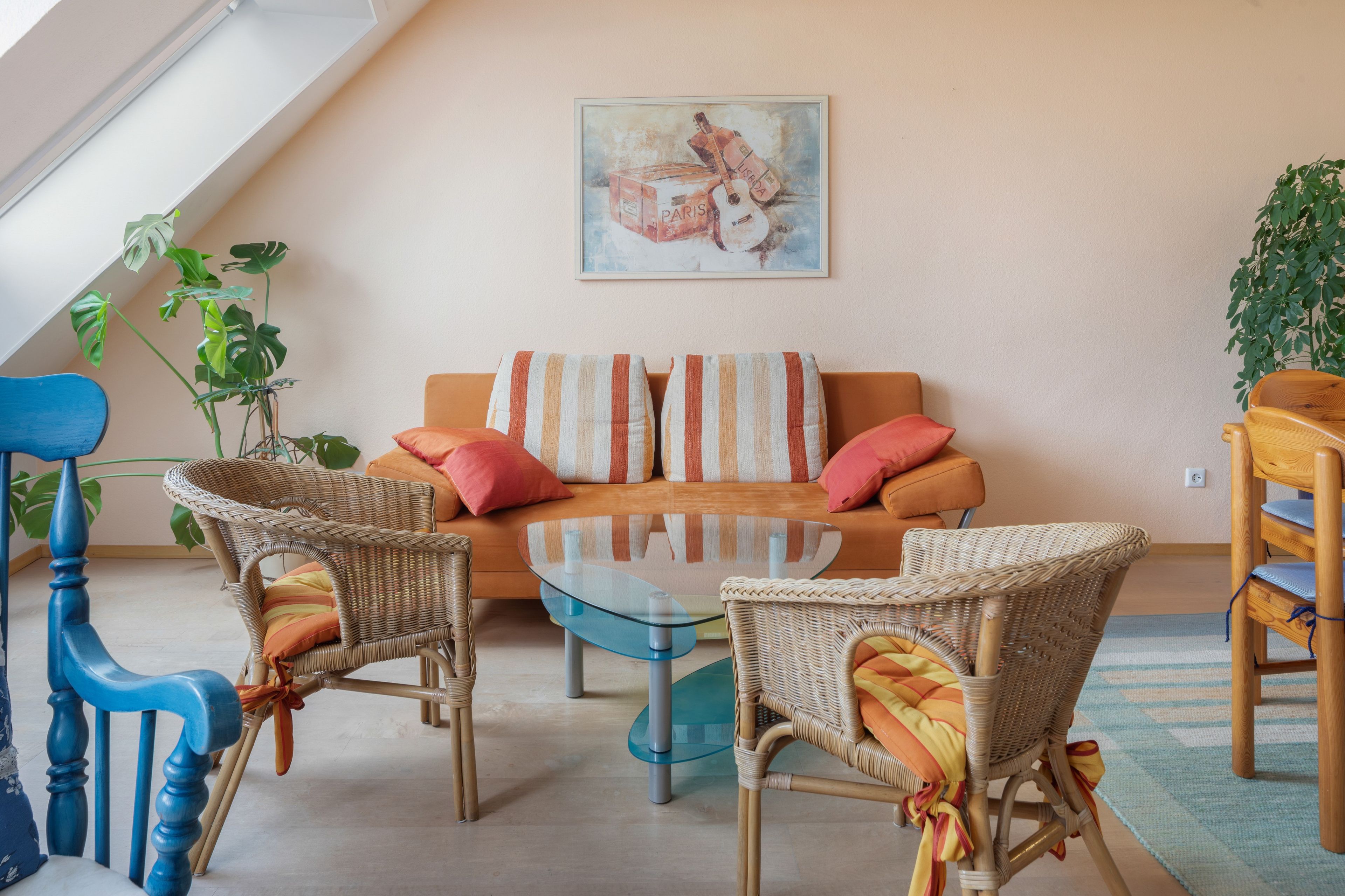 Una sala de estar acogedora con un sofá, dos sillones de mimbre, una mesa de centro de vidrio y un cuadro en la pared.