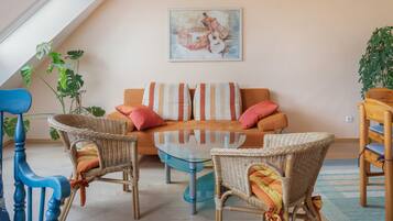 Una sala de estar acogedora con un sofá, dos sillones de mimbre, una mesa de centro de vidrio y un cuadro en la pared.
