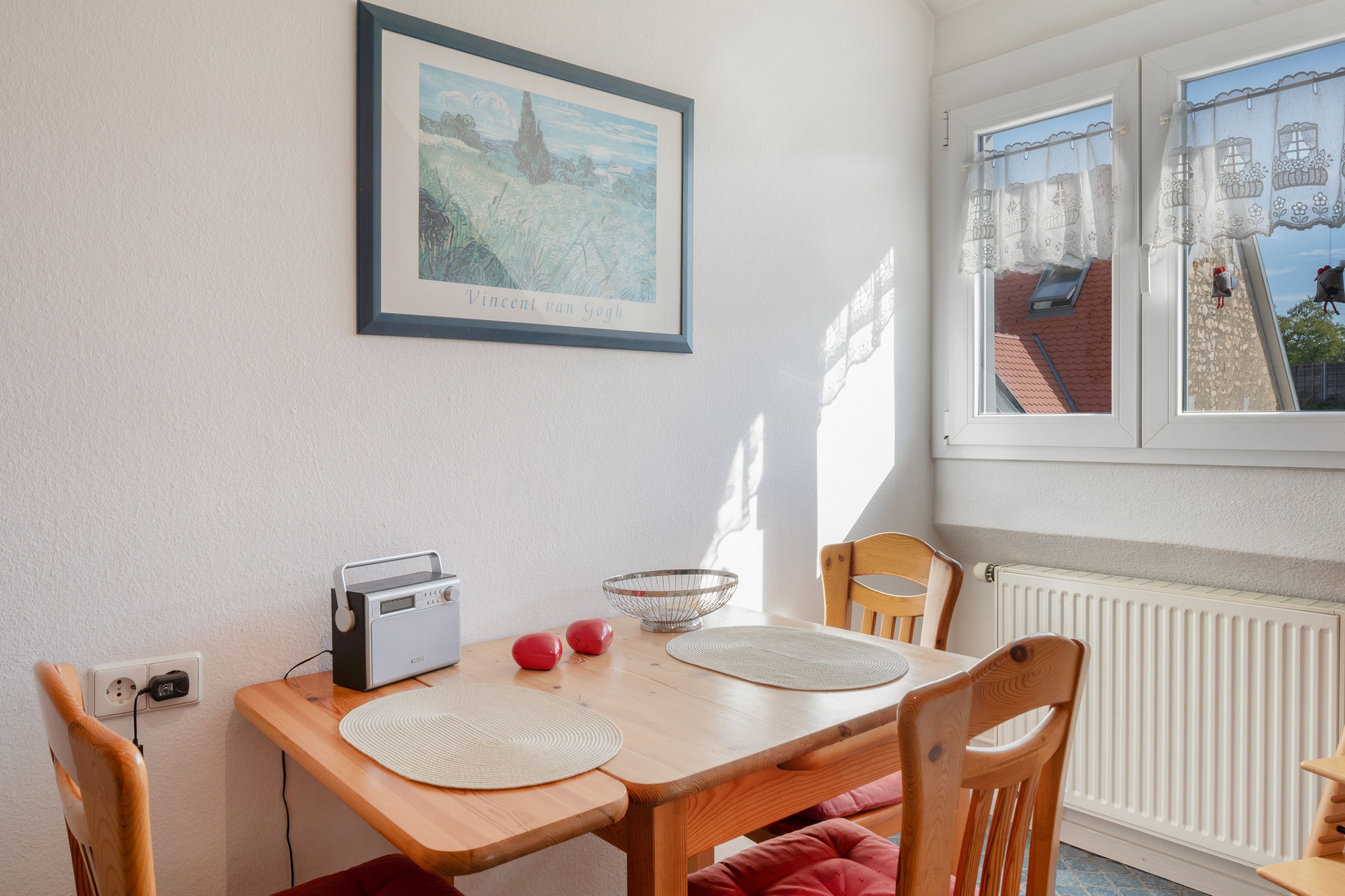 Ein Essbereich mit Tisch, Stühlen, einem Radio und einem gerahmten Gemälde an der Wand.