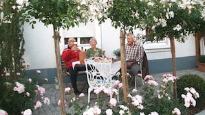 A patio area with a table and chairs, surrounded by flowering plants and a white fence. - Apartment Marlies in Freiburg (Freiburg im Breisgau)