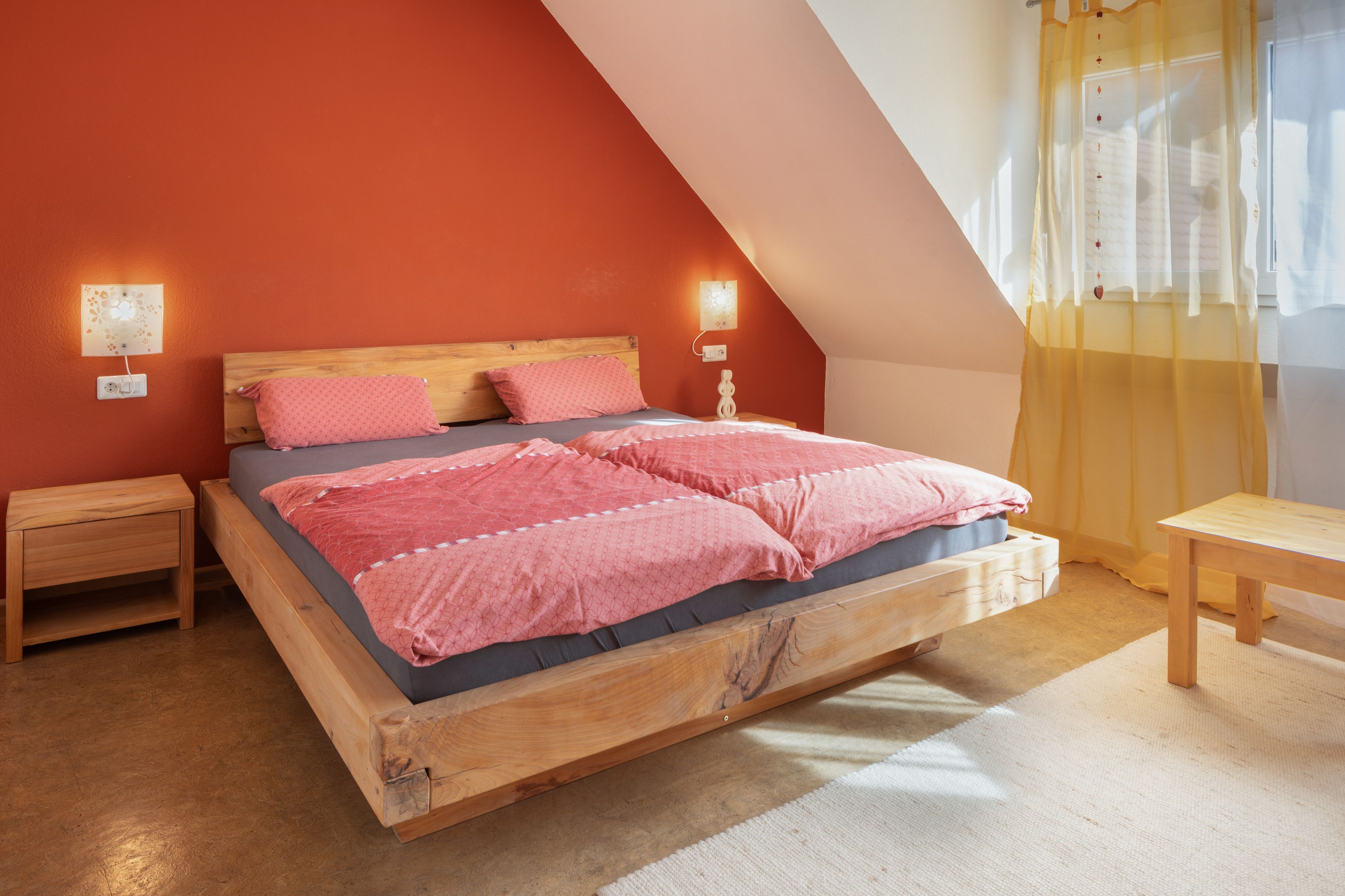Ein Schlafzimmer mit schrägem Dach, einem Holzbettgestell, zwei Nachttischen und einer Nachttischlampe.