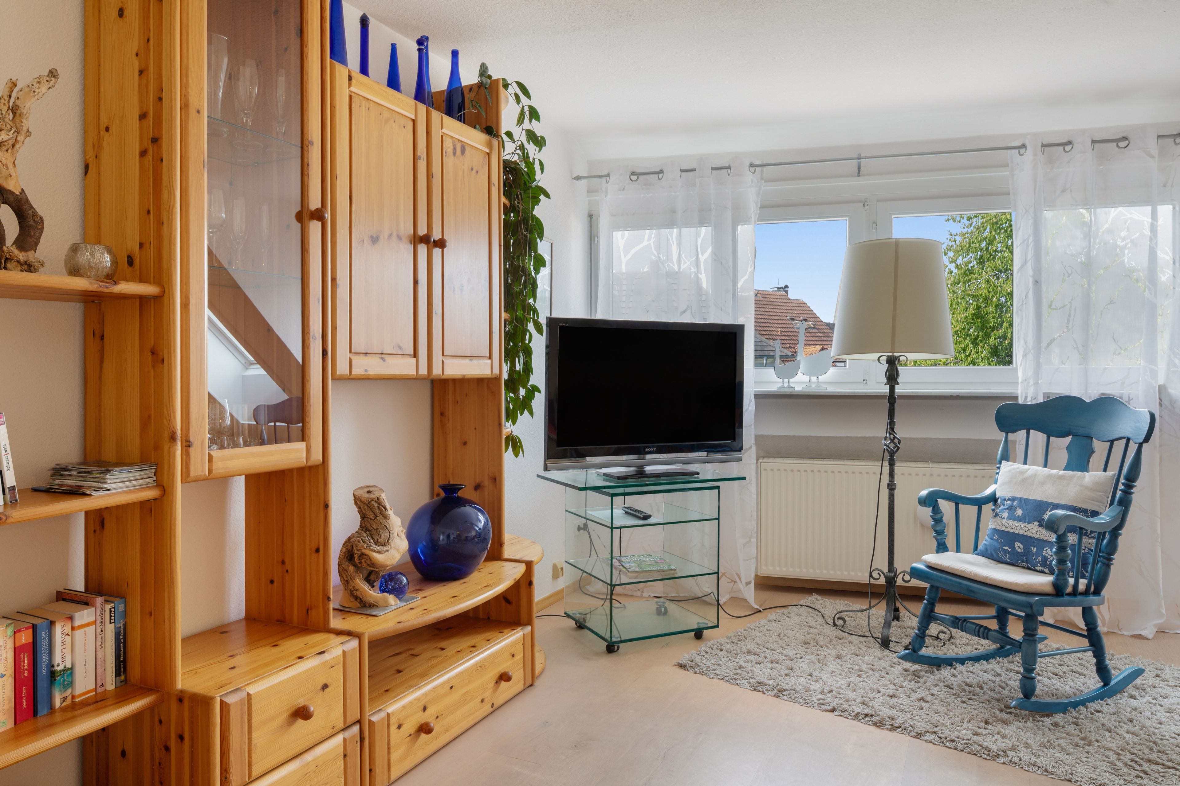 Ein Wohnzimmer mit Fernseher, Holzmöbeln, einem Schaukelstuhl und einem fenster mit Vorhängen.