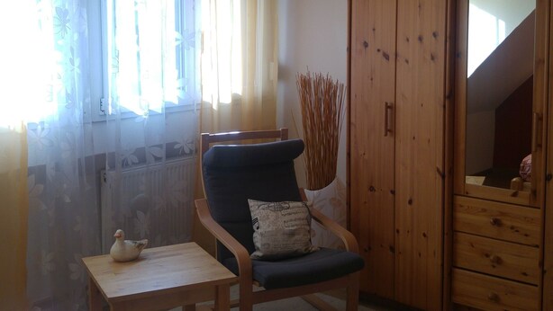 A room with a bed, a chair with a cushion, a small table with a teapot, and a wardrobe. - Apartment Marlies in Freiburg (Freiburg im Breisgau)
