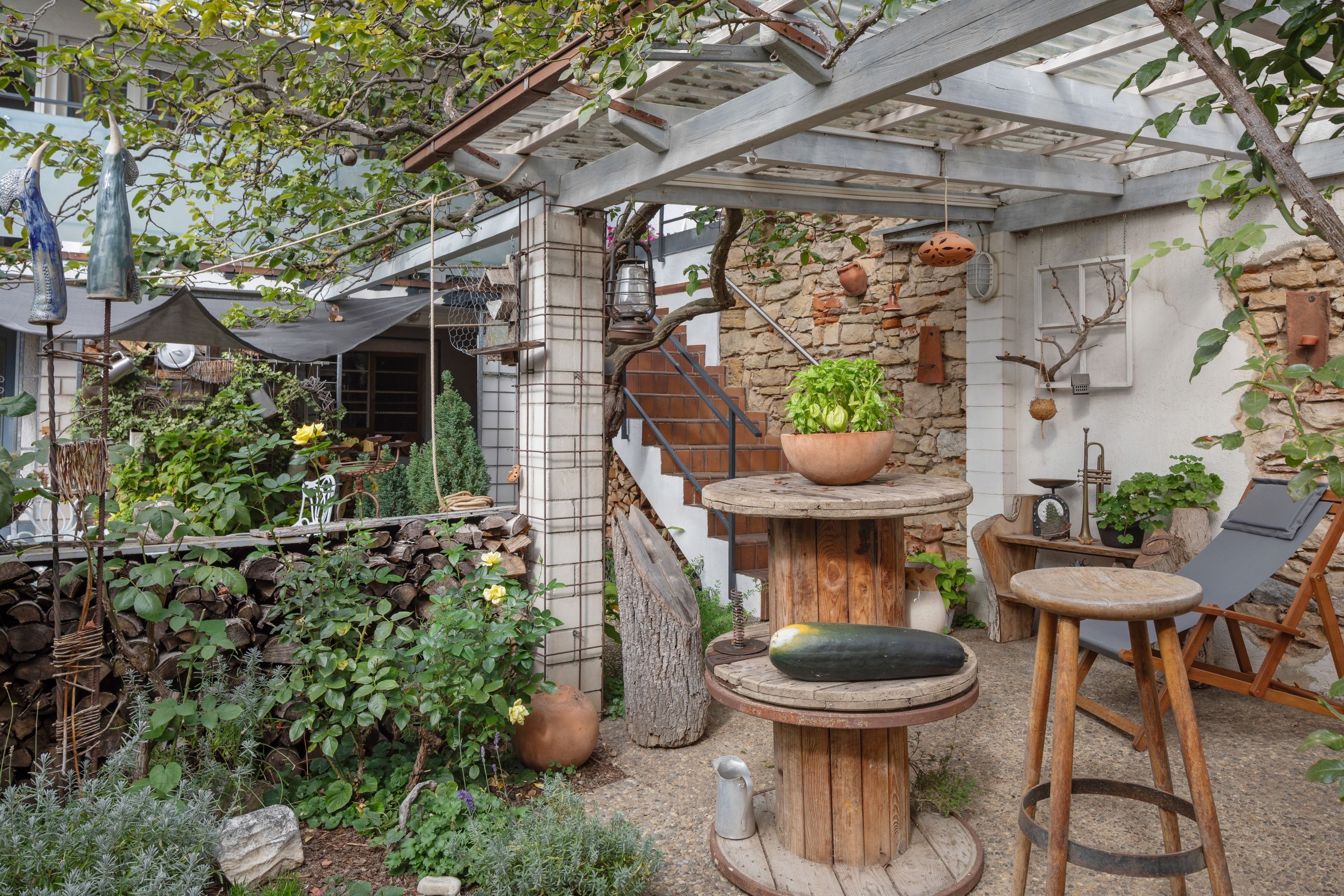 Un espacio de estar al aire libre rústico con una mesa y sillas de madera, rodeado de follaje y un muro de piedra.
