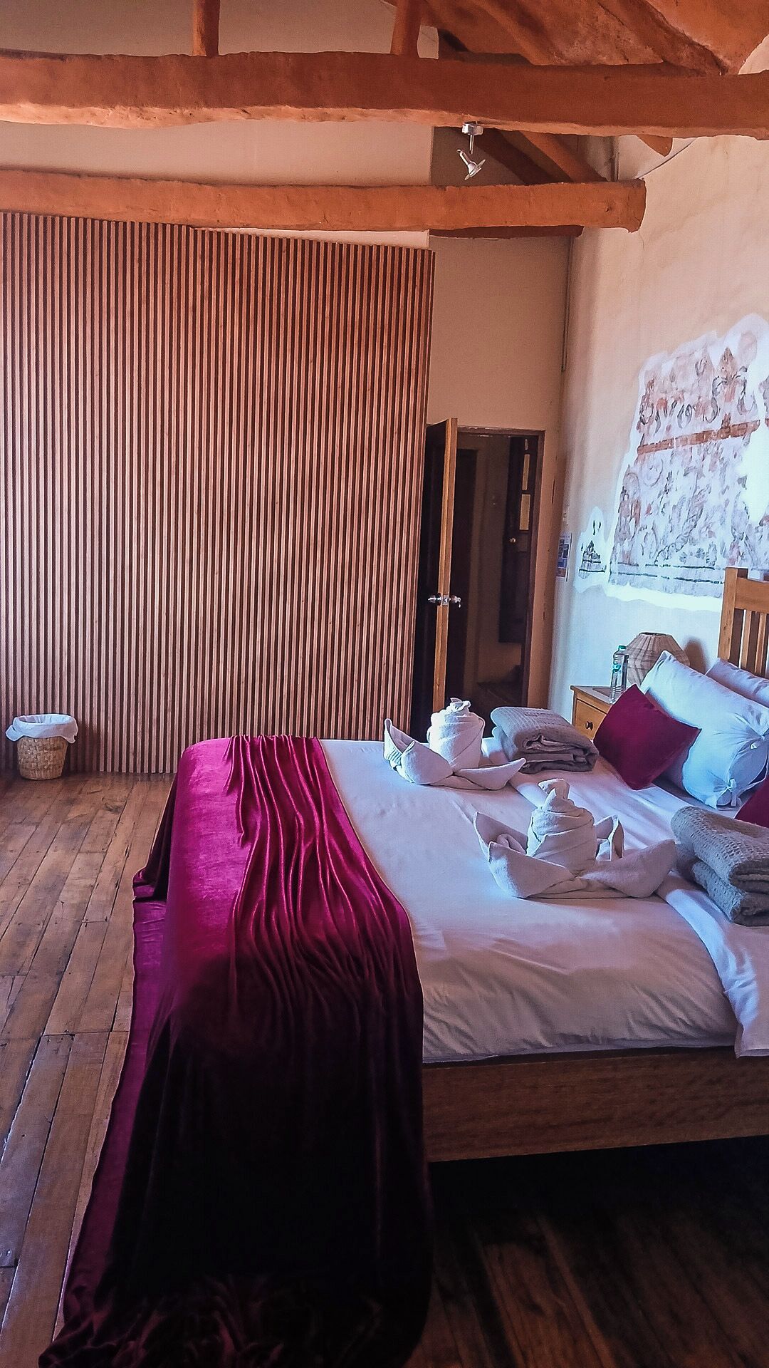 Un dormitorio con cama de madera, una manta roja y suelo de madera.