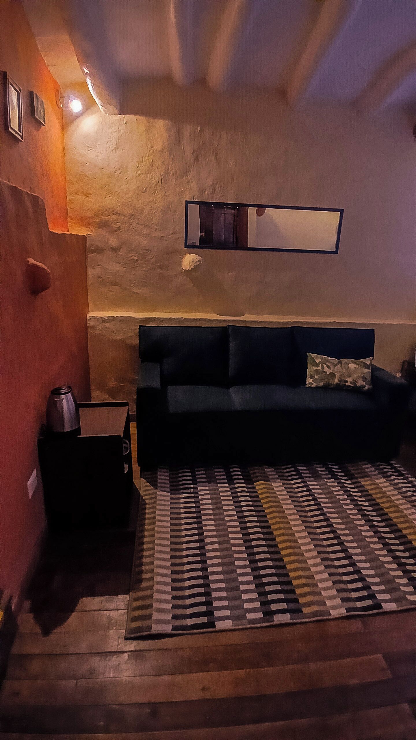 Una habitación con un sofá, un tapete estampado, una mesita y un espejo colgado en la pared.