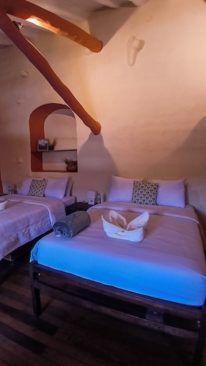 Una habitación con dos camas, un banco de madera, una mesita y un estante en la pared con un cuadro.