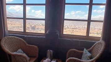 Una habitación con dos sillones de mimbre, una mesita con teteras, y vistas a un paisaje desértico a través de amplias ventanas arqueadas.
