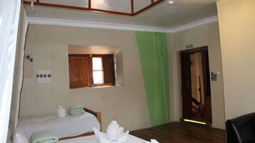 Habitación de hotel con dos camas, un ventanal pequeño, una pared de acento verde y una puerta señalizada con 'SALIDA'.