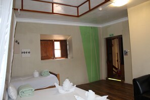 A hotel room with two beds, a small window, a green accent wall, and a door marked 'SALIDA'. - Loki Boutique Cusco (Cusco)