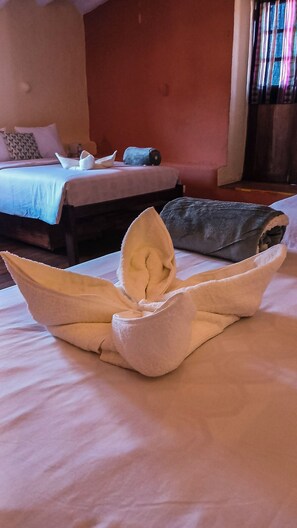 Una cama bien hecha con una toalla doblada en forma de barco, una almohada y un edredón enrollado sobre la cama.