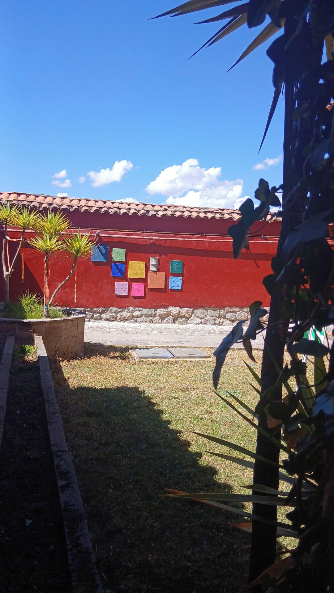 A red building with a tiled roof, a stone wall, and colorful paper notes attached to it.