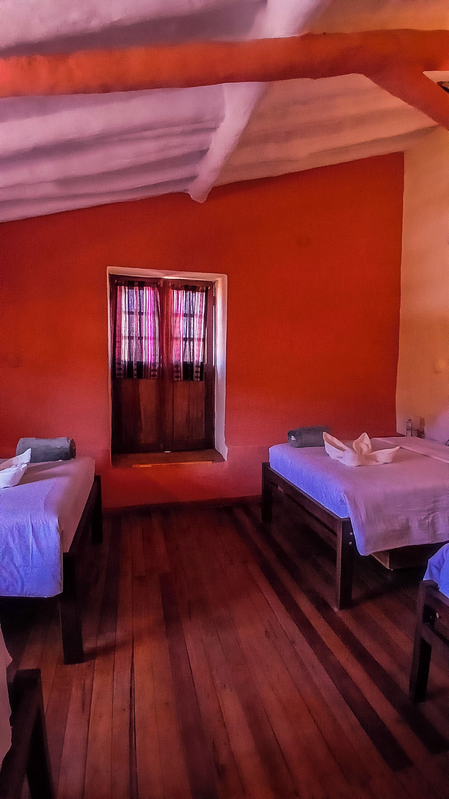 Una habitación con dos camas, una ventana con cortinas y suelo de madera.