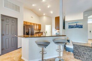 A modern kitchen with a central island, bar stools, and a cityscape painting on the wall. - Merrimack Place (Davenport)