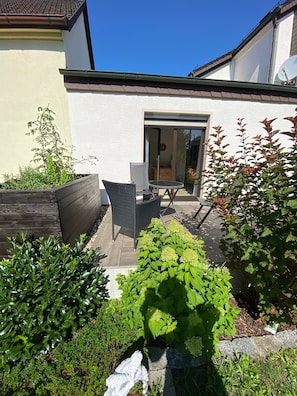 Eine Terrasse mit Tisch und Stühlen, umgeben von Pflanzen und einem Holzbeet.