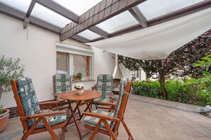 A patio with a table and four chairs, a potted plant, and a window with a view of greenery. - Holiday Apartment "Auszeit" with Private Terrace, Garden, and Wi-Fi (Bad Liebenwerda)