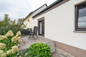 A patio with a table and chairs, a small garden with hydrangeas, and a white building with a window. - Holiday Apartment "Auszeit" with Private Terrace, Garden, and Wi-Fi (Bad Liebenwerda)