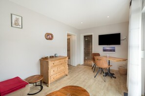 A modern room with a wooden dresser, a dining table with chairs, a television mounted on the wall, and a shower area. - Holiday Apartment "Auszeit" with Private Terrace, Garden, and Wi-Fi (Bad Liebenwerda)