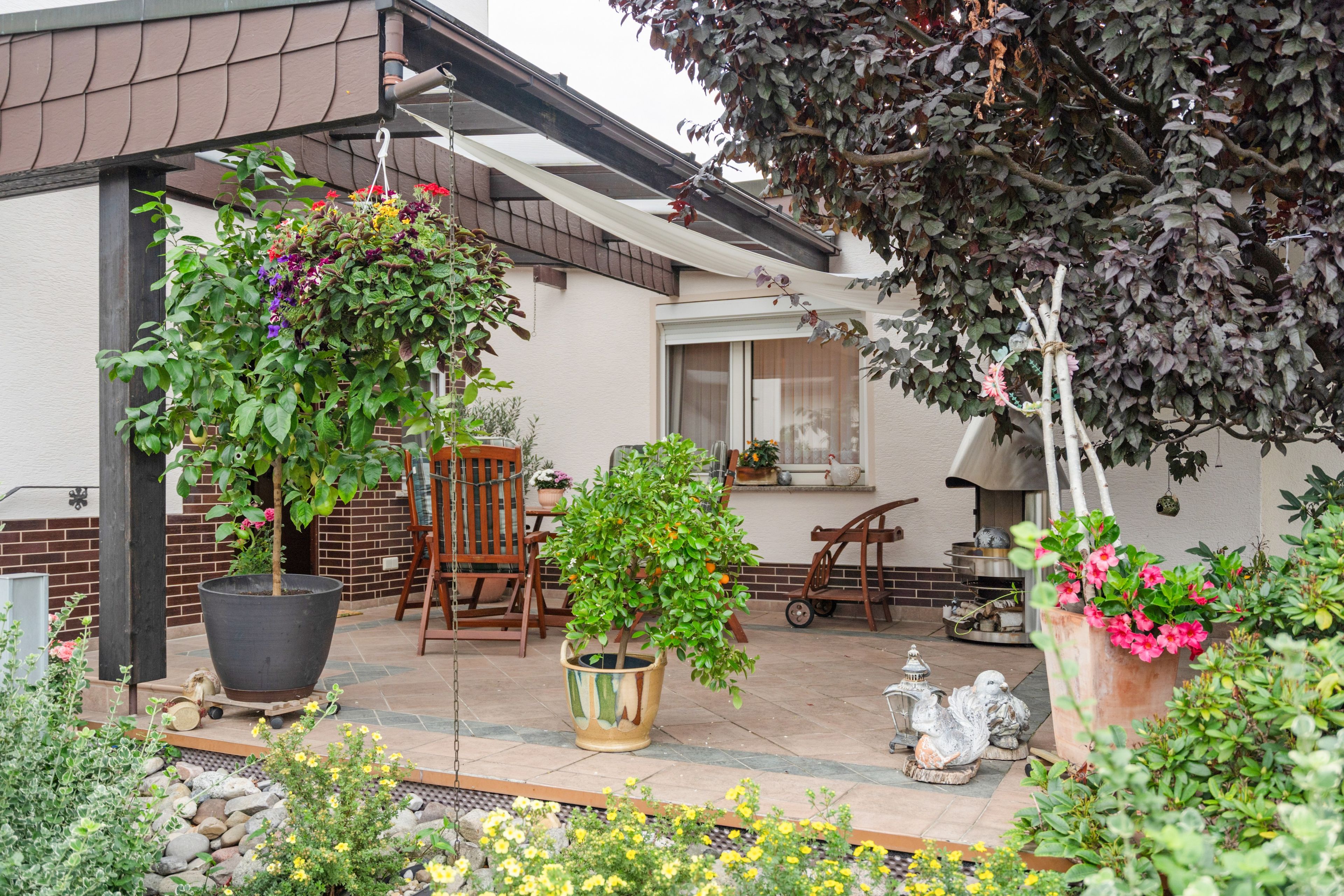 A patio with potted plants, a wooden chair, a table, and a decorative bird sculpture.