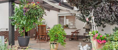 Un patio con plantas en macetas, una silla de madera, una mesa y una escultura decorativa de un pájaro.