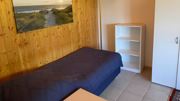 Una habitación con una cama, un armario blanco, una estantería blanca y un cuadro de paisaje colgado en la pared.