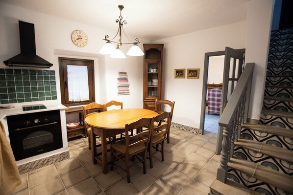 A kitchen with a dining table, chairs, a clock, a cabinet, and a staircase.