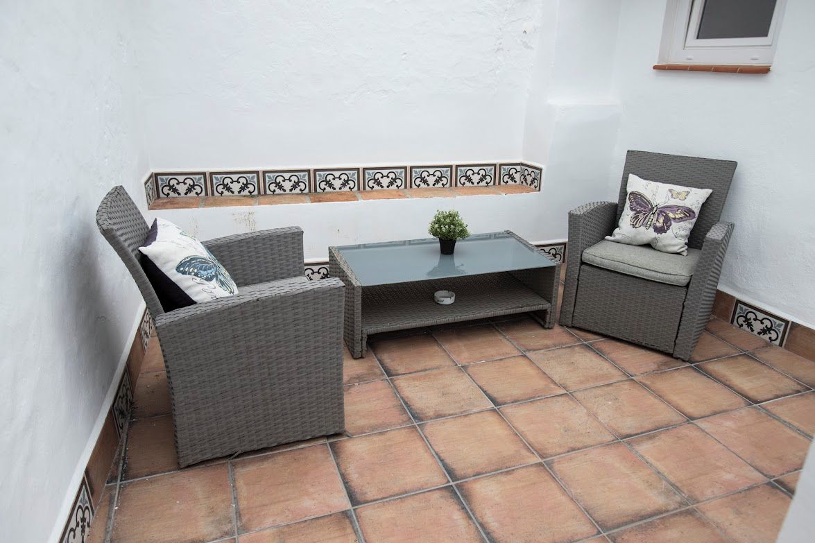 A small patio area with wicker furniture, a tiled floor, and a decorative tile border.