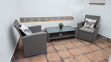 A small patio area with wicker furniture, a tiled floor, and a decorative tile border.