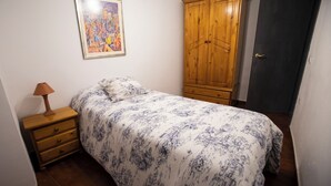 A bedroom with a bed, a wooden wardrobe, a nightstand with a lamp, and a framed picture on the wall. - Casa rural La Bandolera (Grazalema)