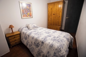 A bedroom with a bed, a wooden wardrobe, a nightstand with a lamp, and a framed picture on the wall.