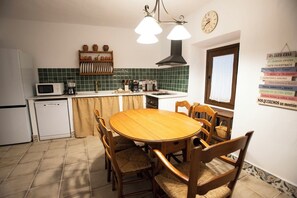 Una cocina con una mesa redonda de madera, sillas, un microondas, una cafetera y un reloj en la pared.