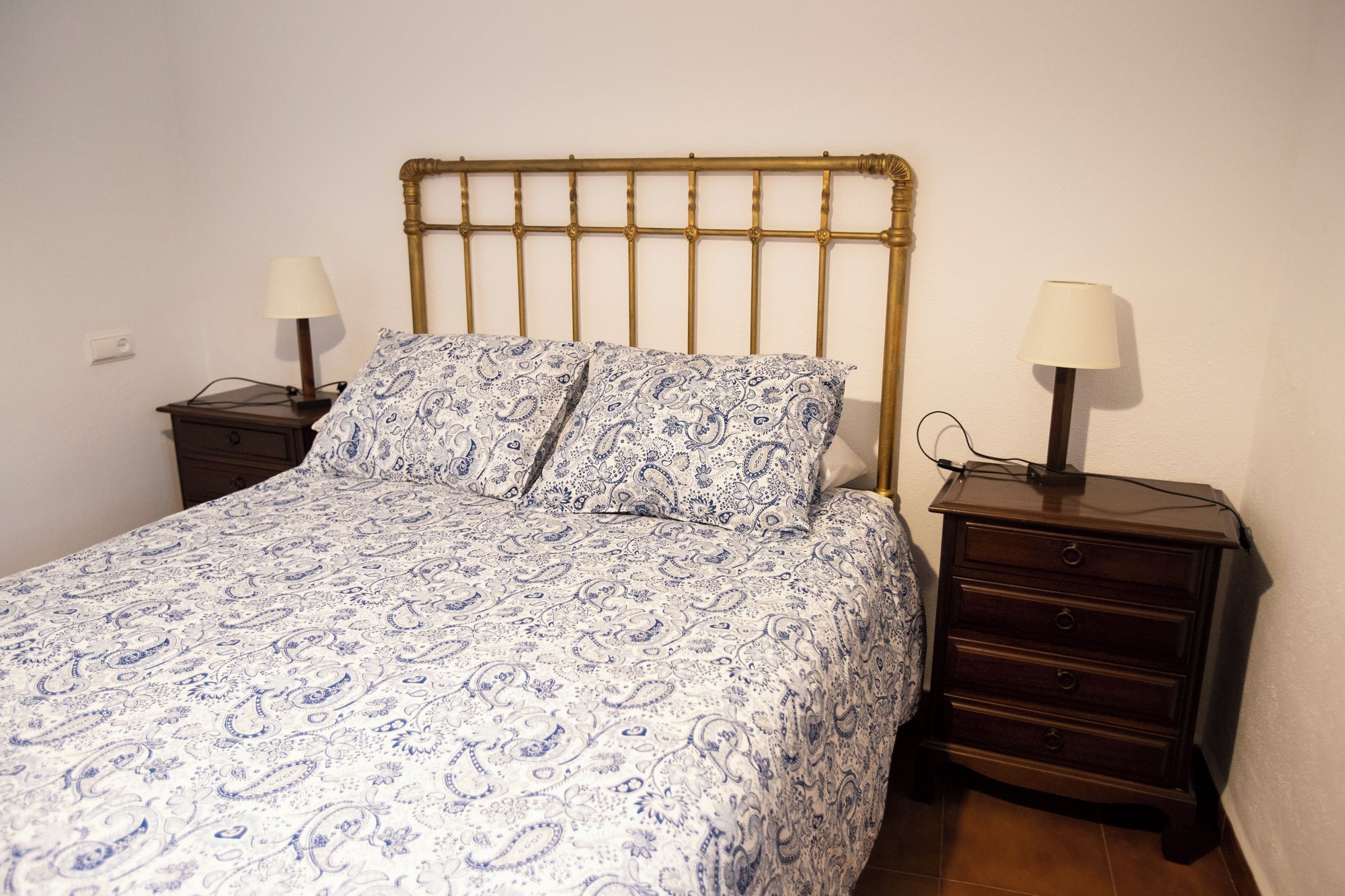 A single bed with a patterned bedspread, two bedside tables with lamps, and a wooden headboard.