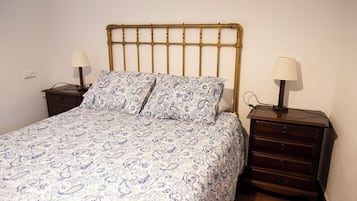 A single bed with a patterned bedspread, two bedside tables with lamps, and a wooden headboard.