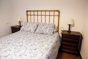 A single bed with a patterned bedspread, two bedside tables with lamps, and a wooden headboard.
