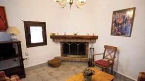 A cozy room with a fireplace, a wooden table with a plant, a chair, a lamp, and a framed picture on the wall. - Casa rural La Bandolera (Grazalema)