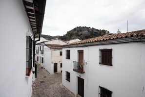 A narrow street with white buildings, a cobblestone path, and a hill in the background.