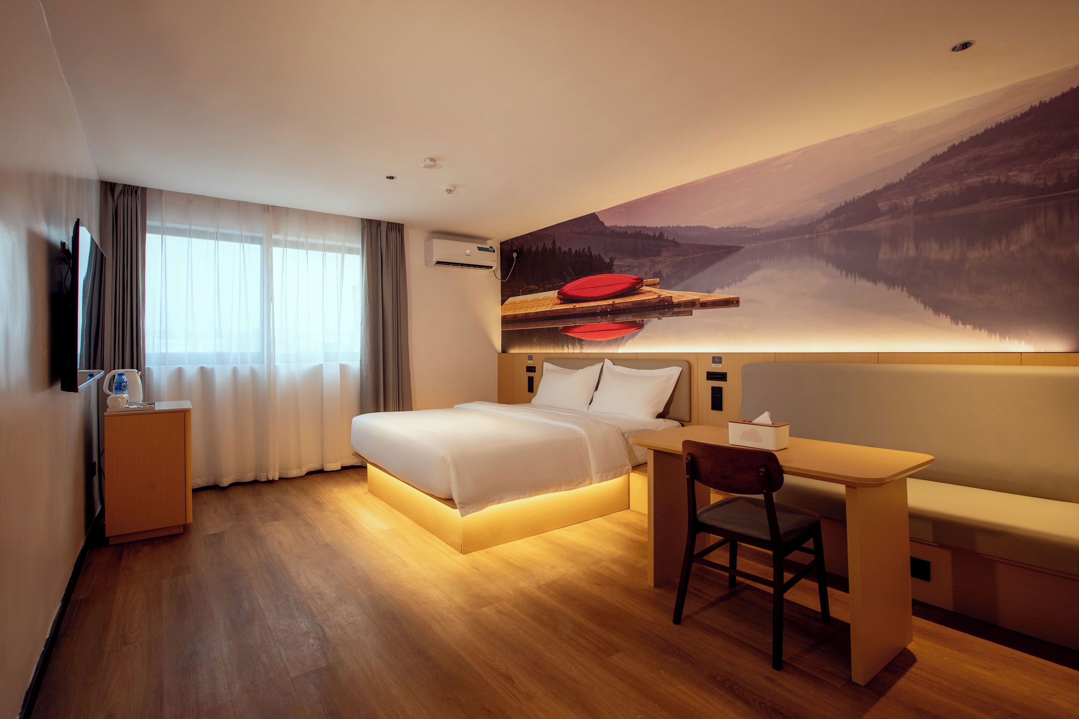 Ein Hotelzimmer mit Bett, Schreibtisch, Stuhl und einem Gemälde einer Berglandschaft.